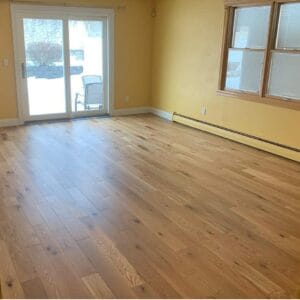 Hardwood floor installation in a sunlit room with sliding doors and yellow walls.