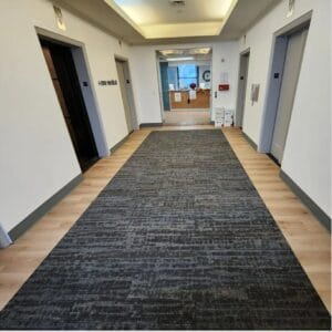 Hallway with light wood-look luxury vinyl tile flooring and dark grey patterned carpet tile runner.